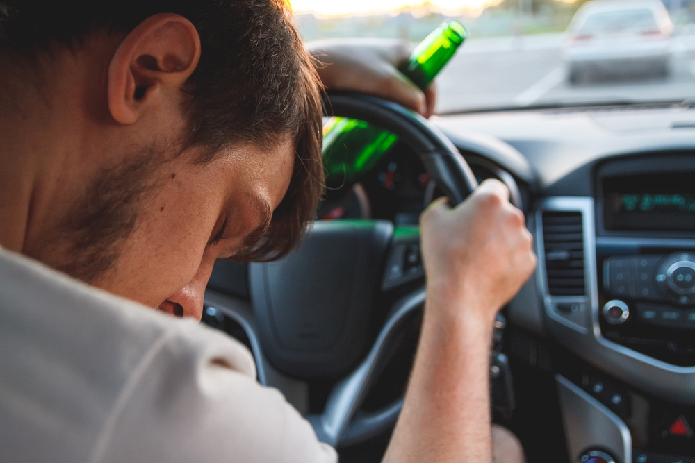 drunk young man driving a car with a bottle of beer
