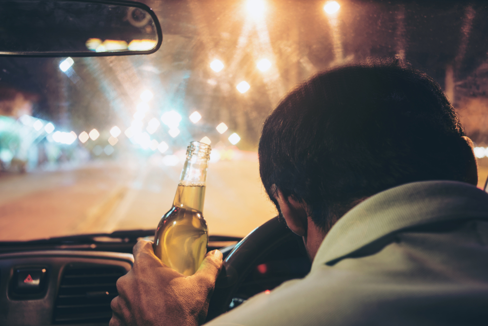 drunk young man drives a car with a bottle of beer